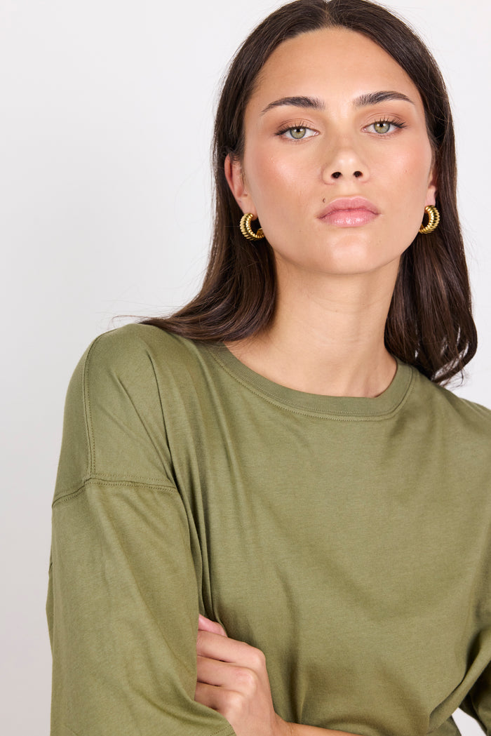 Woman wearing an olive green short-sleeve top against a white background