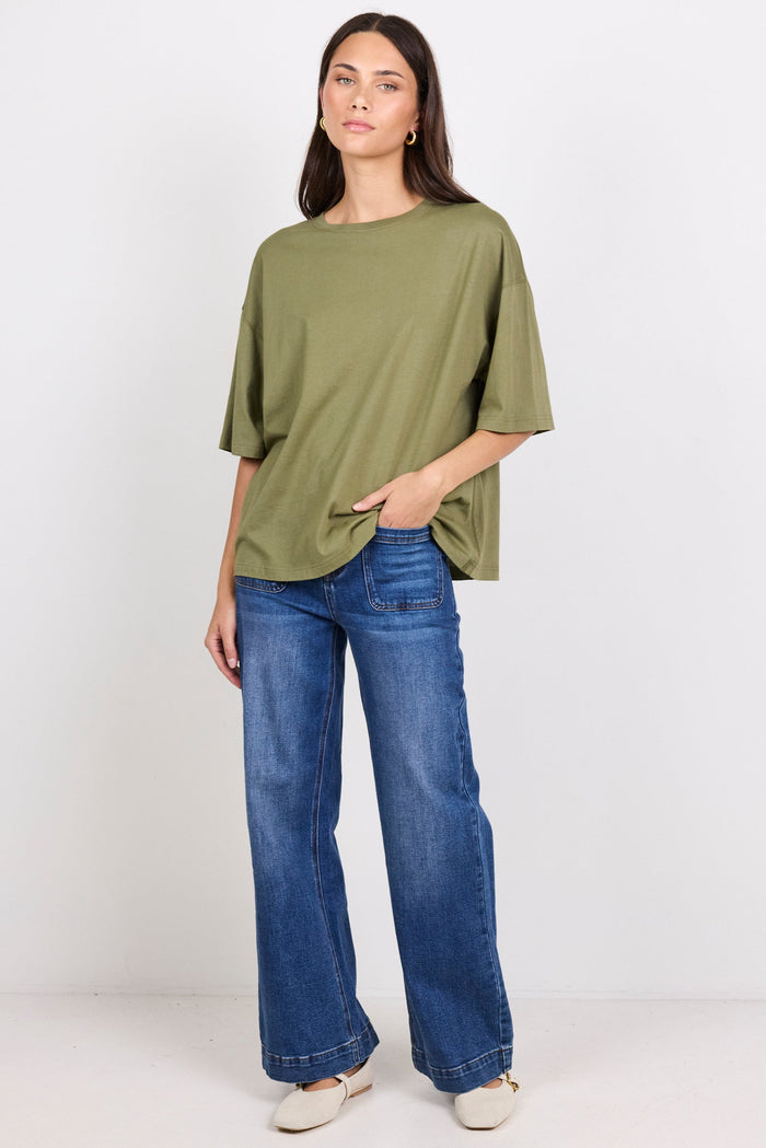 Woman wearing a green oversized shirt and blue jeans on a white background