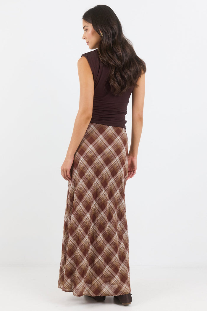 Woman wearing a long patterned skirt and brown top on a white background