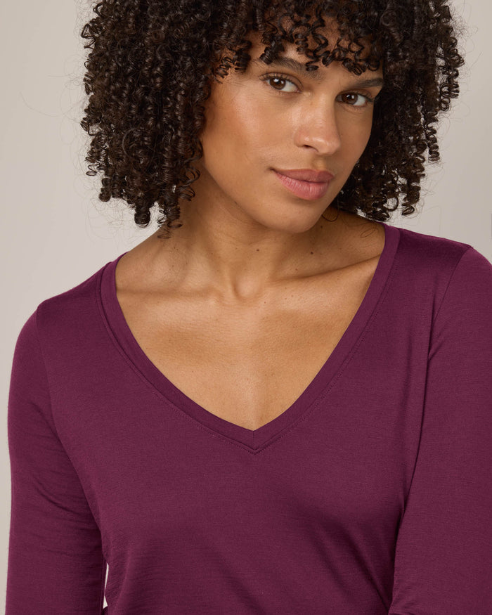 Model wearing Brenton V-Neck Tee in Plum, a warm purple-red color. Brenton V-Neck Tee is a merino wool long sleeve, v-neck, regular fit tee available in sizes XS-3X.