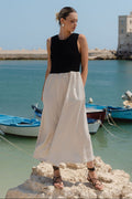 Woman standing on rocks by a harbor with boats and a clear sky