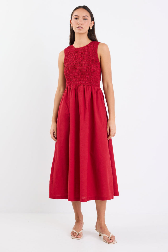 Woman wearing a sleeveless plum midi dress with a shirred bodice, crew neckline, and gathered flowing skirt.