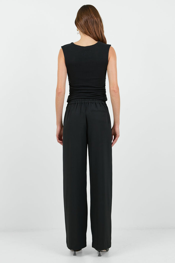 Woman wearing a black sleeveless top and wide-leg pants on a white background