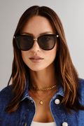 model wears cat-eye sunglasses featuring a sleek black frame paired with khaki-tinted lenses. A slim gold-tone bridge and matching gold arm accents elevate the look with a modern, minimalist touch.
