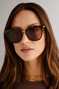 cat-eye sunglasses in a tortoiseshell frame with warm brown lenses. A slim gold-tone bridge and matching gold arms add a polished touch to the bold silhouette.