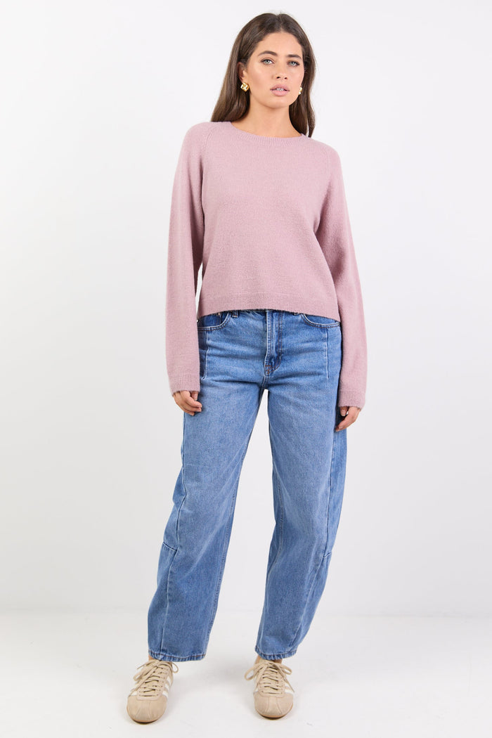 Woman wearing a pink sweater and blue jeans on a white background