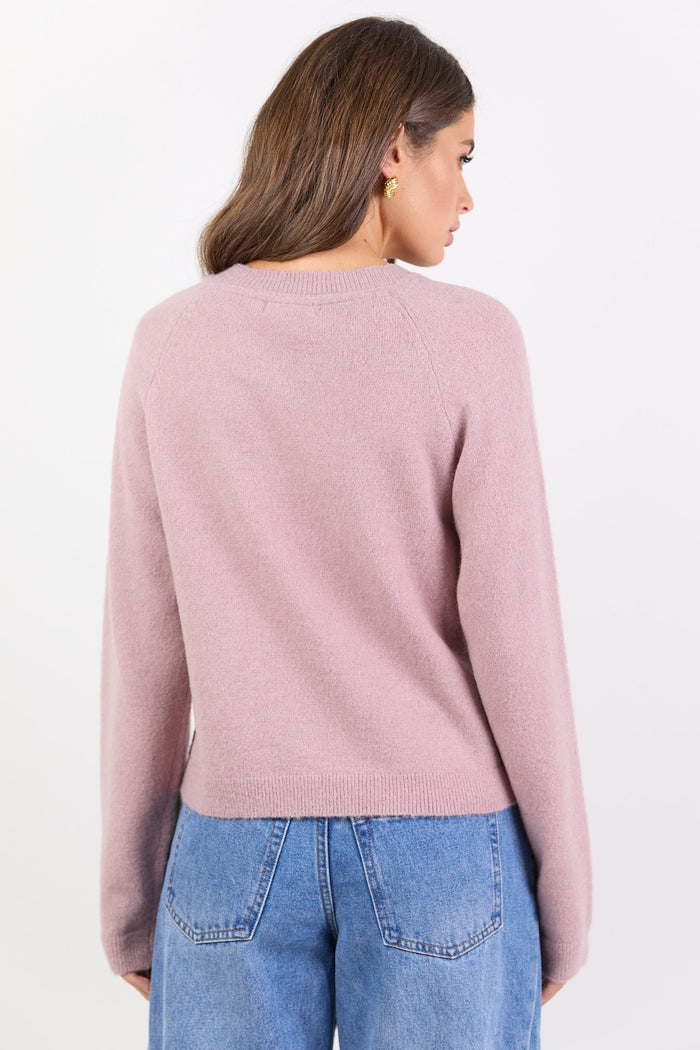 Woman wearing a pink sweater and blue jeans on a white background