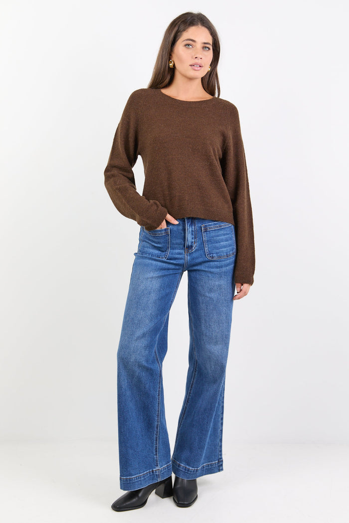 Woman wearing a brown sweater and blue jeans on a white background