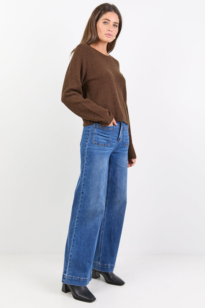 Woman wearing a brown sweater and blue jeans on a white background