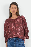 Woman wearing a burgundy floral blouse and blue jeans on a white background