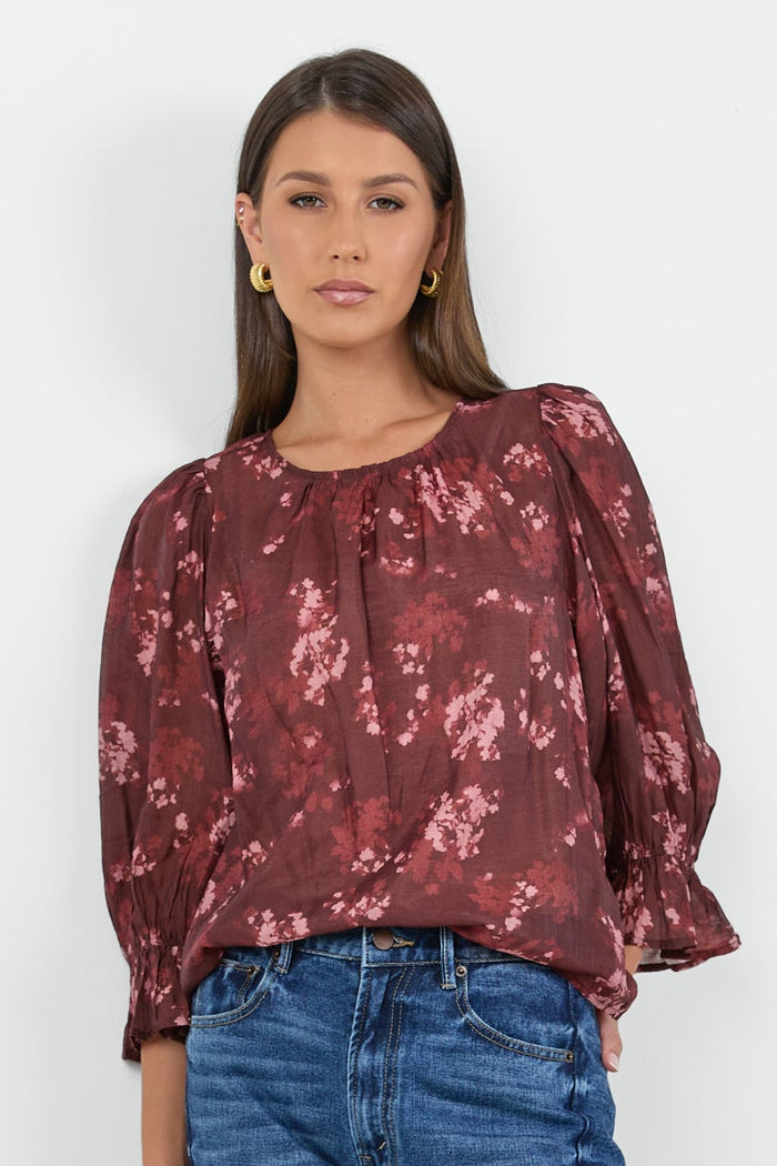 Woman wearing a burgundy floral blouse and blue jeans on a white background