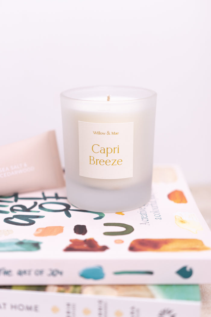 Candle labeled 'Capri Breeze' on a stack of books with a white background