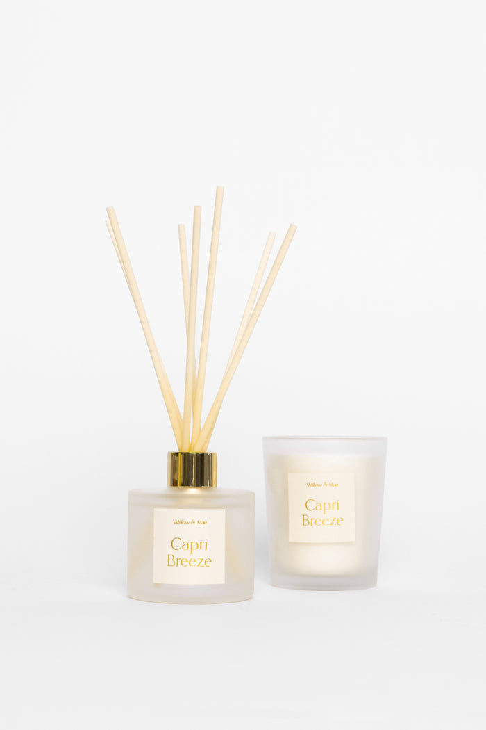 Two diffusers, one with reeds and a candle, on a white background