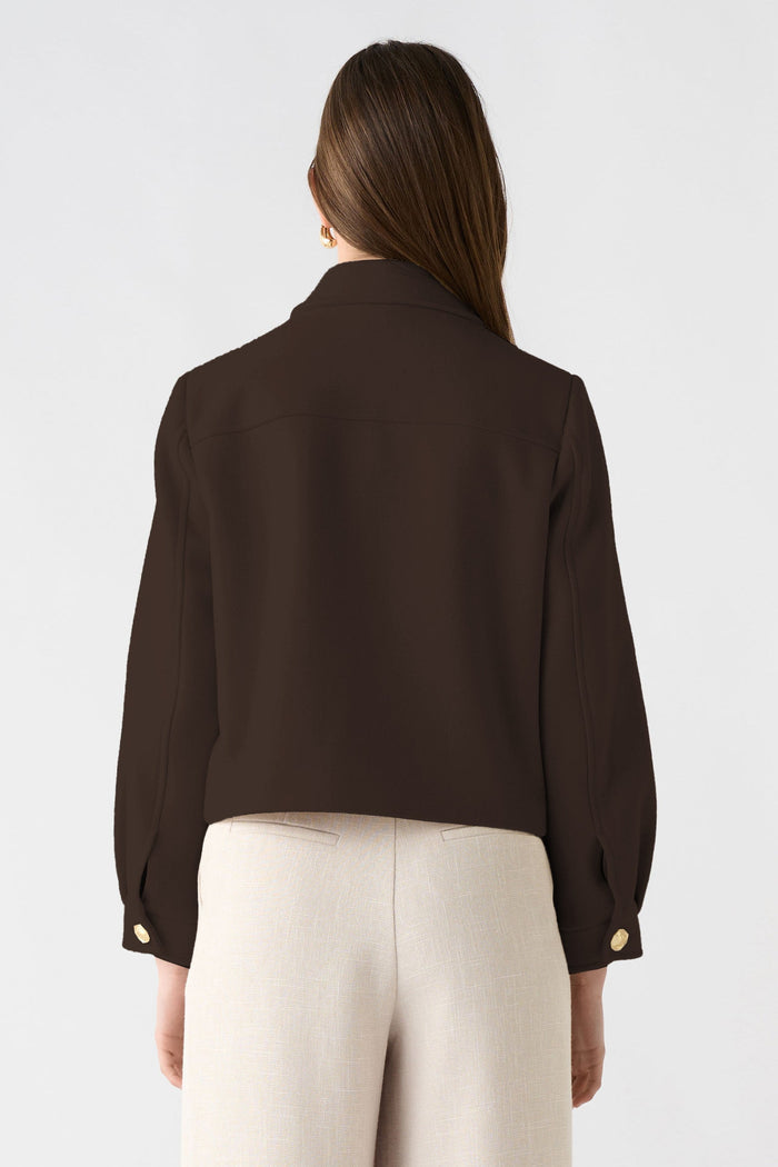 Person wearing a brown blazer and beige pants on a white background