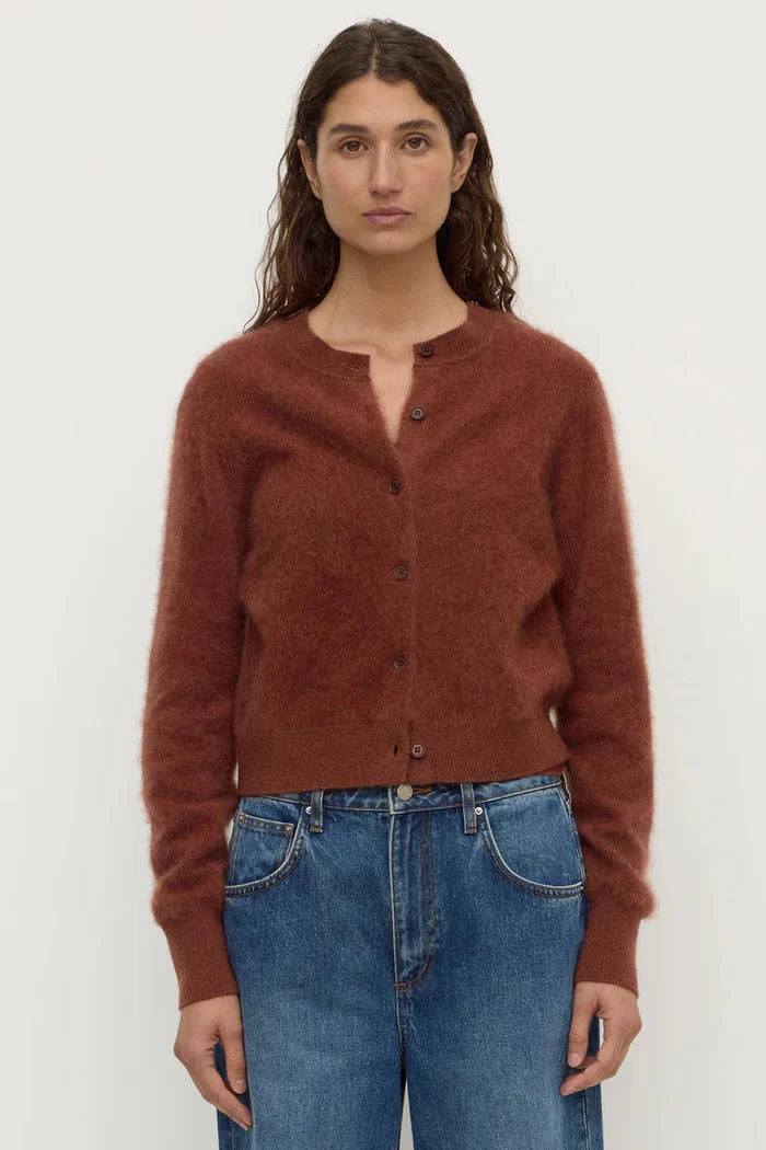 Woman wearing a brown cardigan and blue jeans against a white background