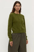 Woman wearing a green cardigan and brown pants on a white background