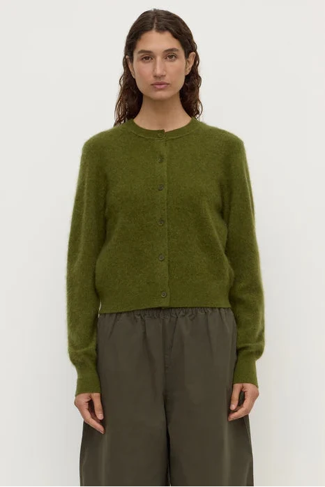 Person wearing a green cardigan and brown pants against a white background