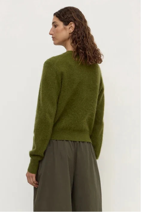 Woman wearing a green sweater and brown pants against a white background