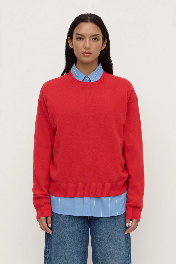 Person wearing a red sweater over a blue shirt and jeans on a white background