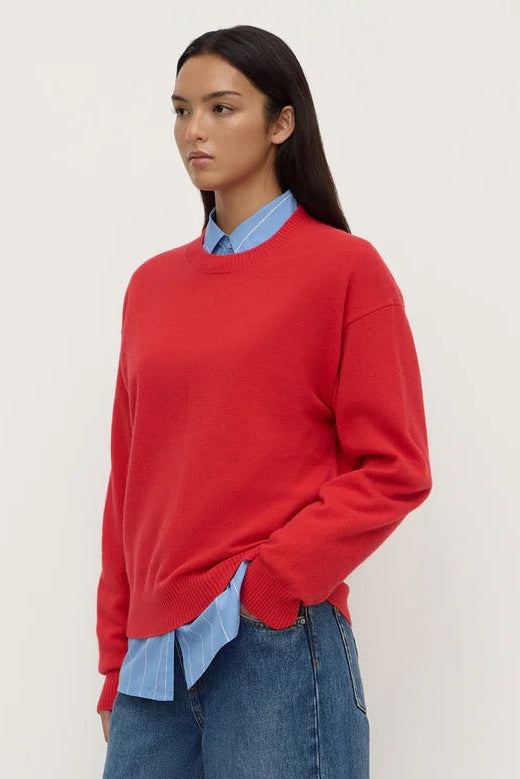 Person wearing a red sweater, light blue shirt, and blue jeans on a white background