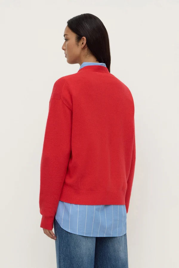Person wearing a red sweater over a blue shirt and jeans on a white background