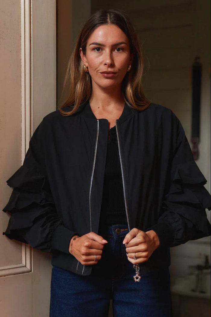 Woman wearing a black jacket and blue pants standing in a room with wooden paneling.