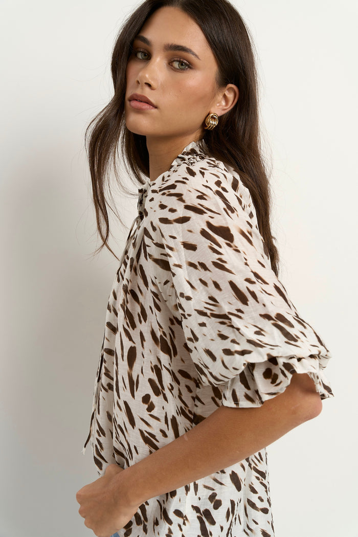 Woman wearing a loose animal-print blouse with ruffled collar and blue wide-leg jeans.