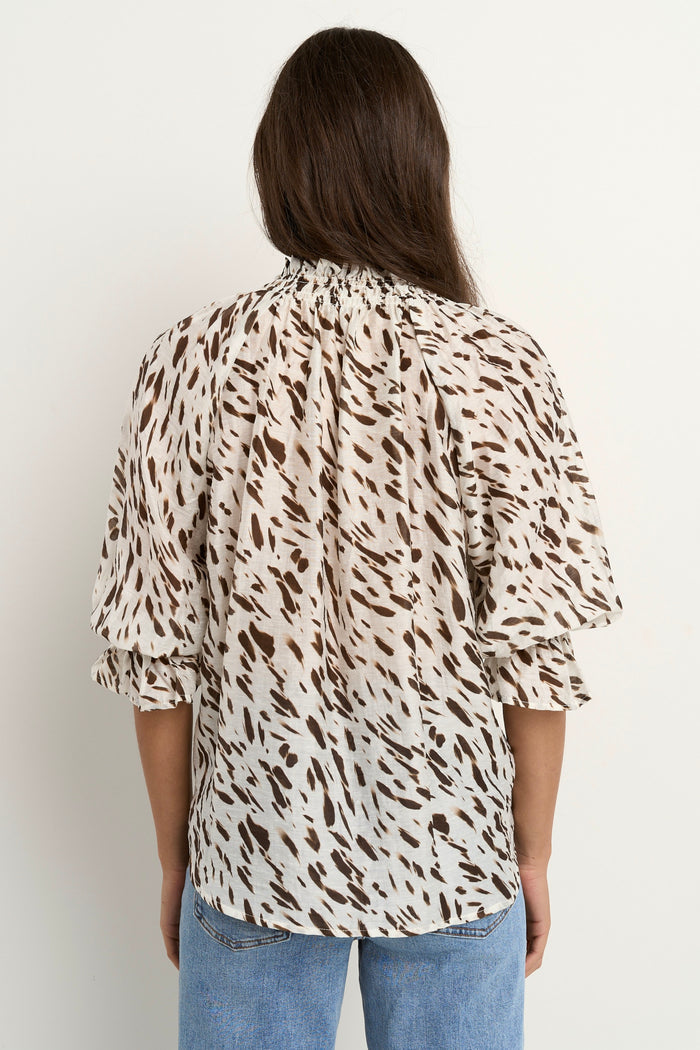 Woman wearing a loose animal-print blouse with ruffled collar and blue wide-leg jeans.