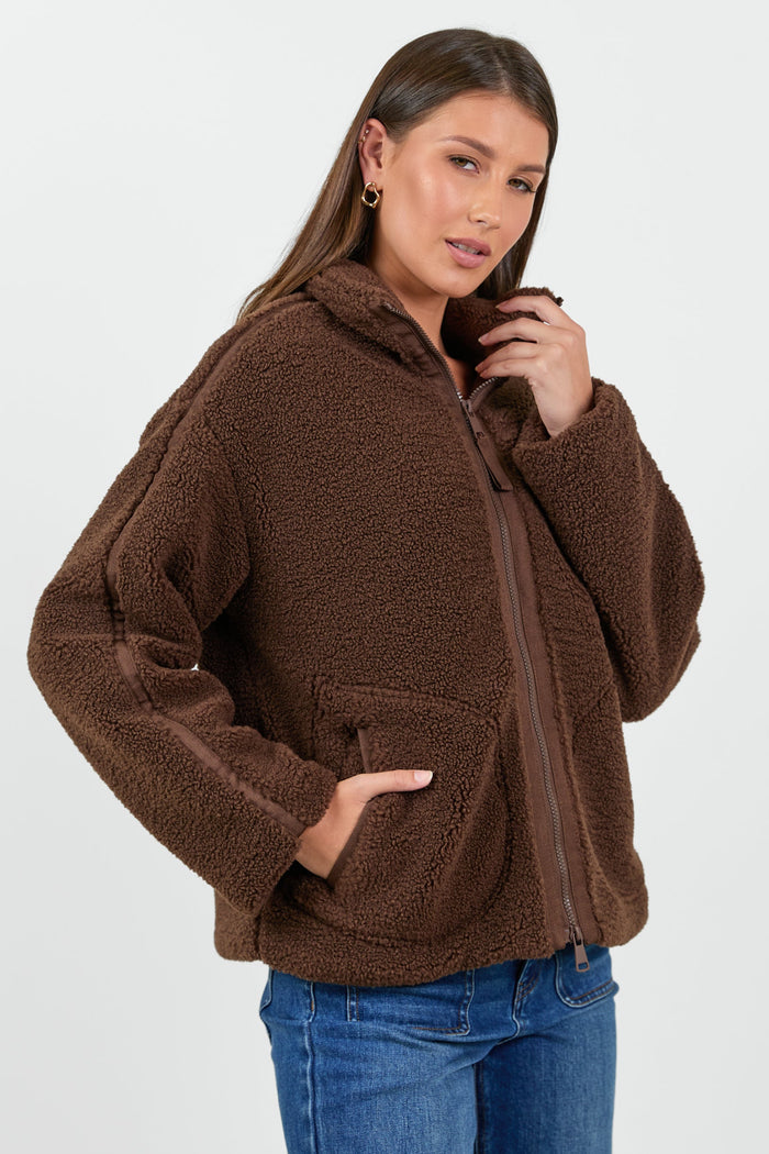 Woman wearing a chocolate brown sherpa fleece zip jacket and blue jean against a white background