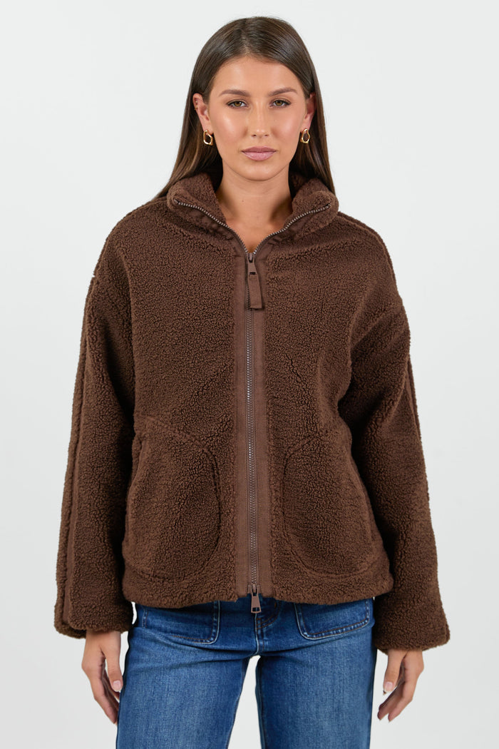 Woman wearing a chocolate brown sherpa fleece zip jacket and blue jean against a white background