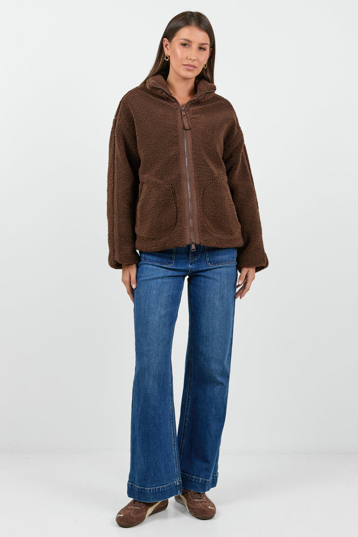 Woman wearing a chocolate brown sherpa fleece zip jacket and blue jean against a white background