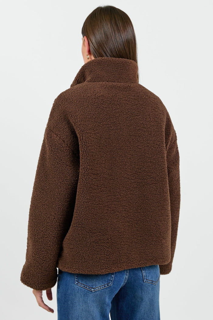 Person wearing a brown jacket and blue jeans on a white background