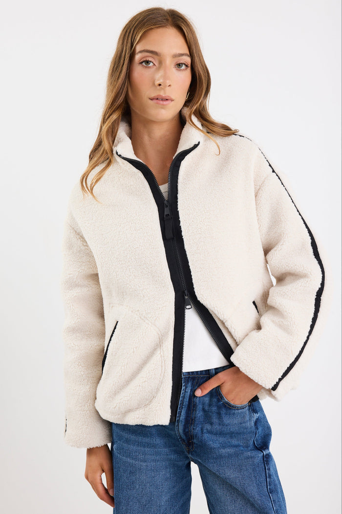 Woman wearing a cream-colored jacket with black trim on a white background