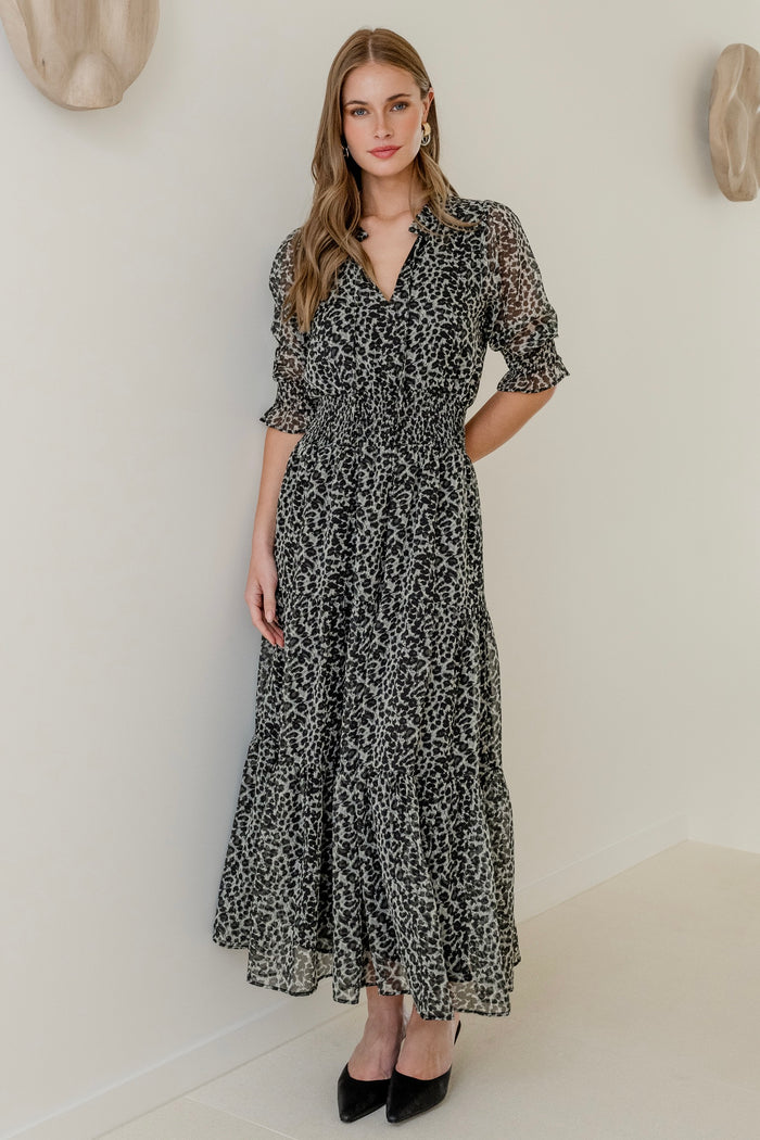 Woman wearing a charcoal animal print short sleeve dress with shirred bodice and tiered skirt, styled with black heels.