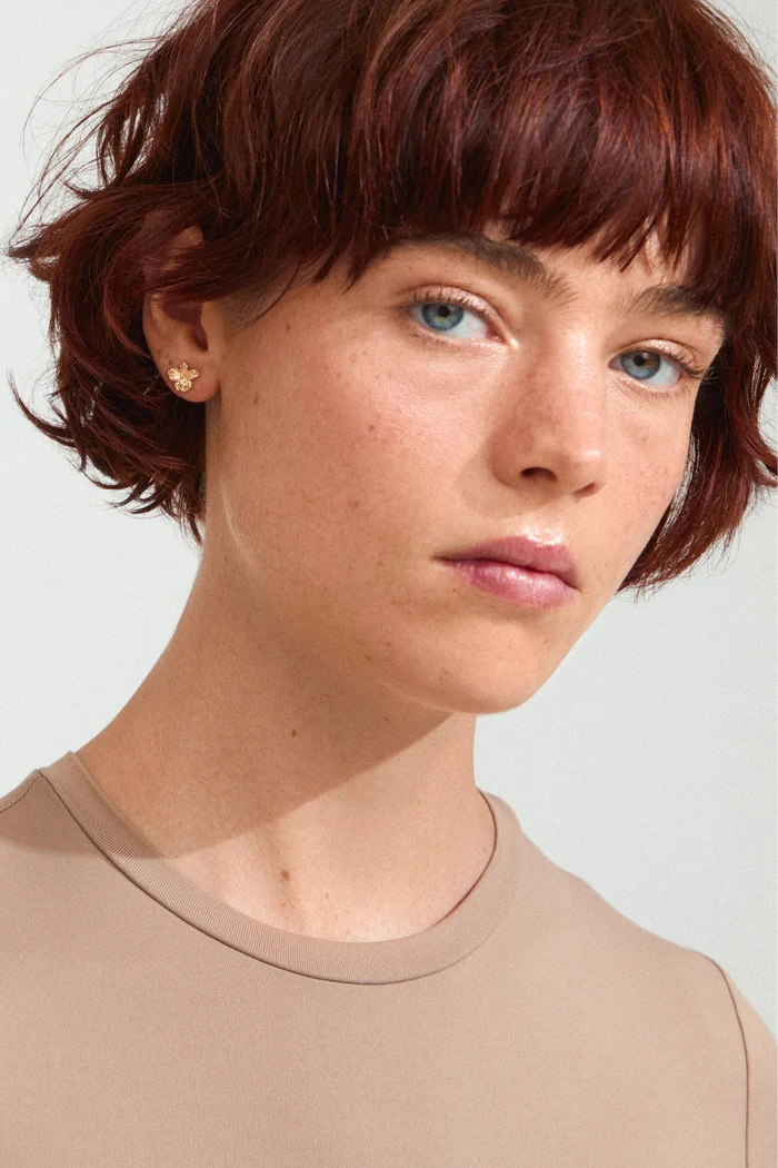 Person with short red hair wearing a beige shirt against a light background