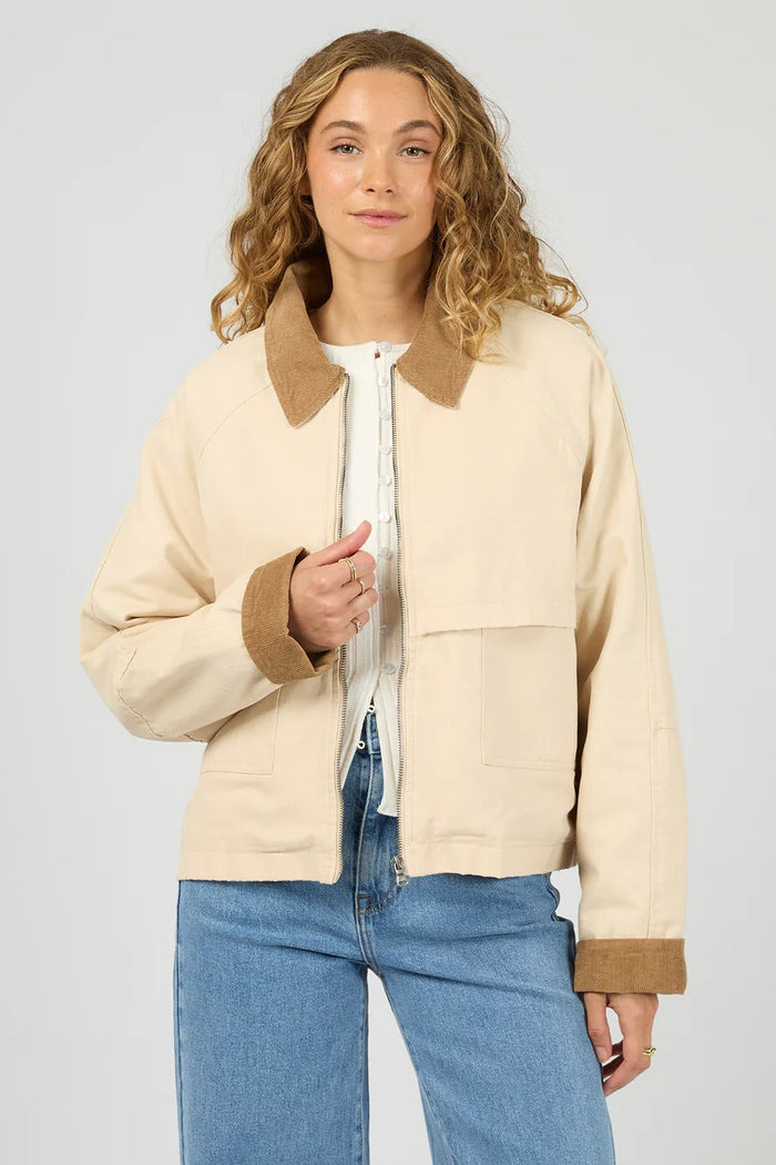 Woman wearing a beige jacket with brown collar and cuffs on a plain background