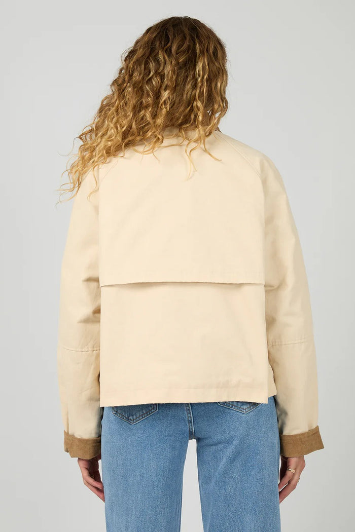 Person wearing a beige jacket and blue jeans on a plain background