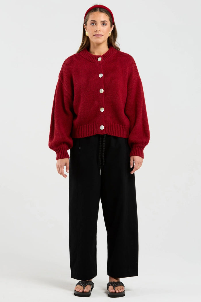 Person wearing a red cardigan and black pants on a white background