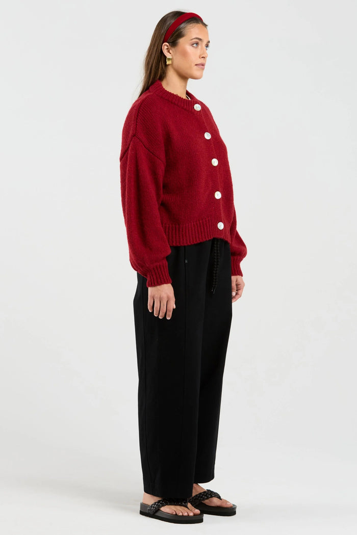 Person wearing a red sweater with white buttons and black pants on a white background