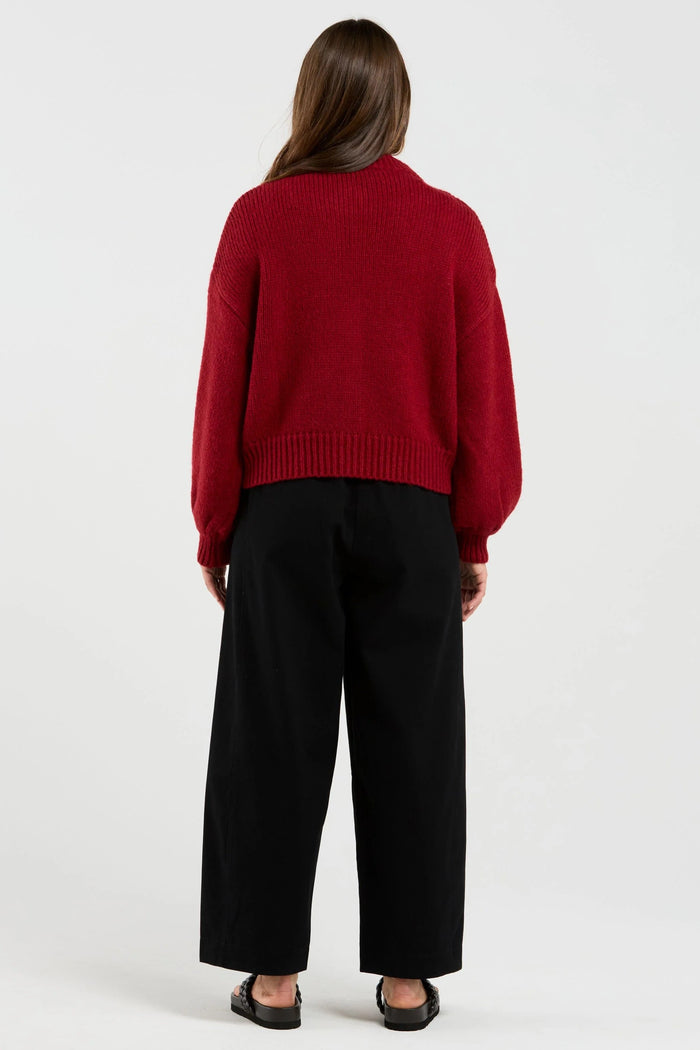 Person wearing a red sweater and black pants on a white background