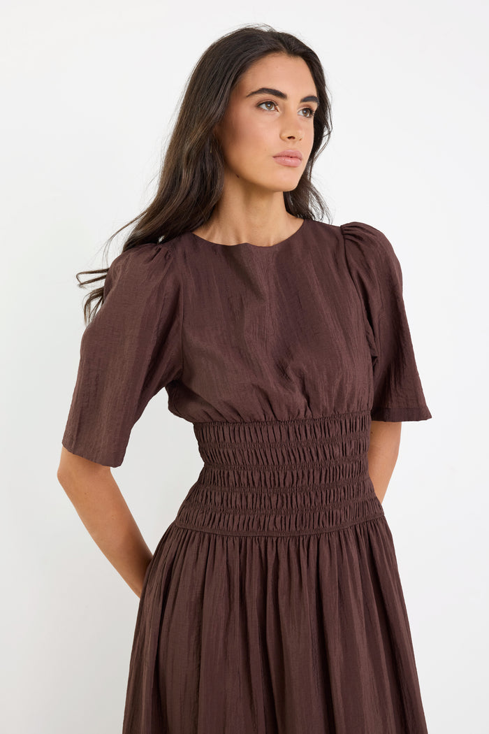 Woman wearing a brown dress with puffed sleeves against a white background