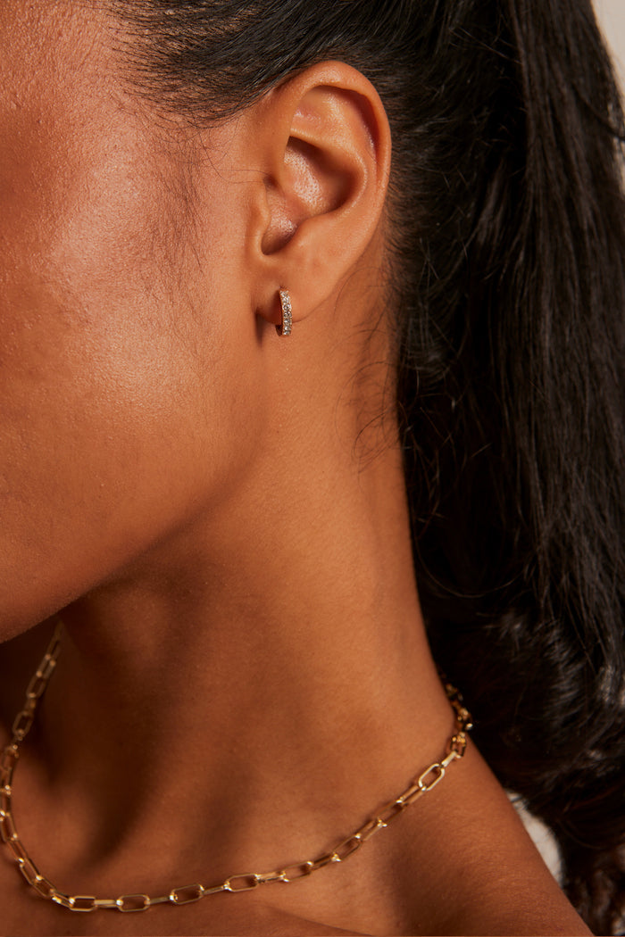 Model wears small diamante hoop earring with a gold chain necklace.