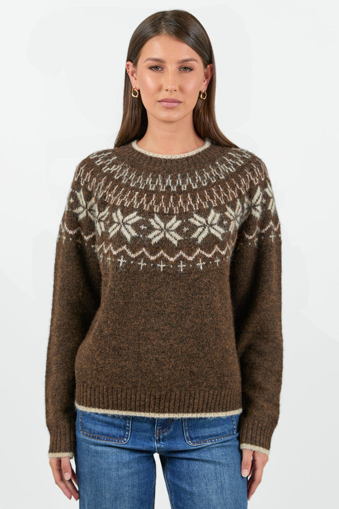 Woman wearing a brown patterned sweater and blue jeans on a white background