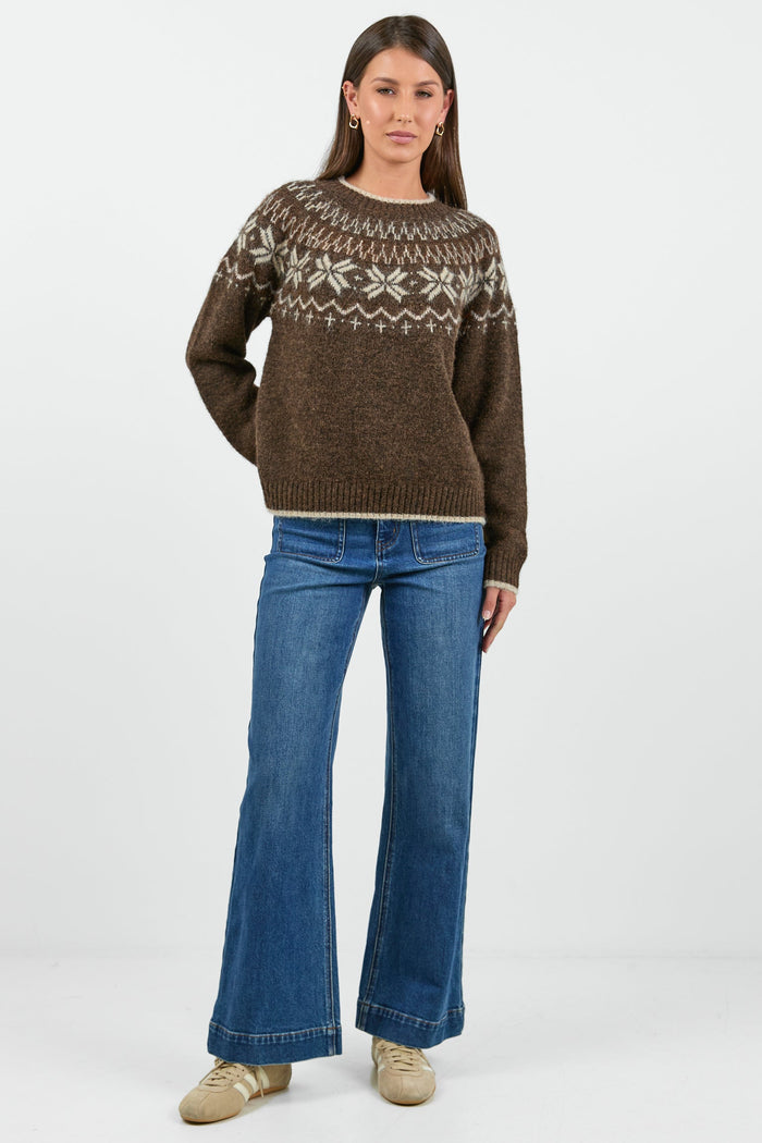 Woman wearing a brown patterned sweater and blue jeans on a white background