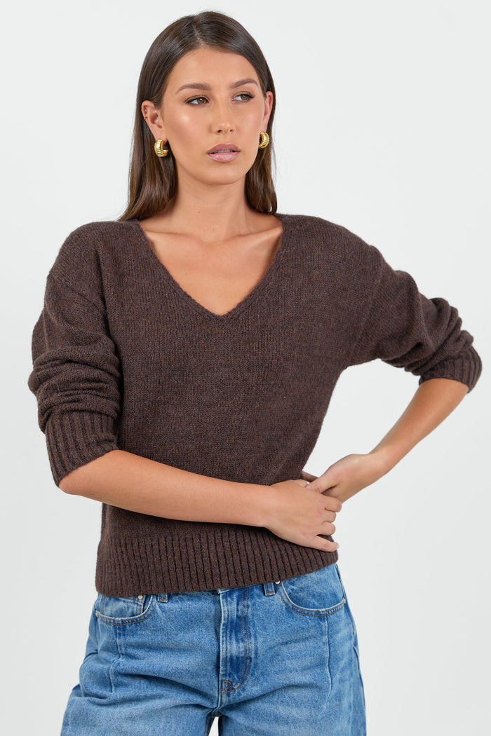 Woman wearing a chocolate brown knit jumper and blue jeans against a white background