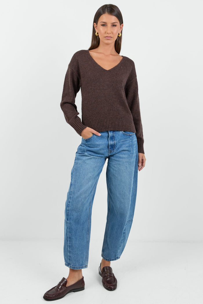 Woman wearing a chocolate brown knit jumper and blue jeans against a white background