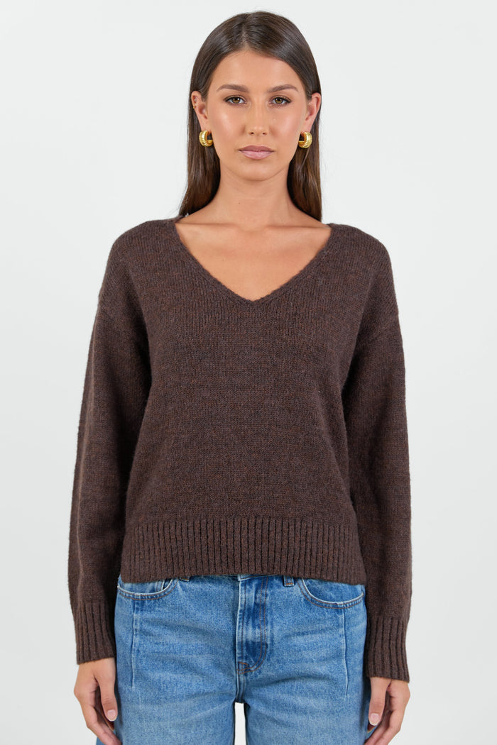 Woman wearing a chocolate brown knit jumper and blue jeans against a white background