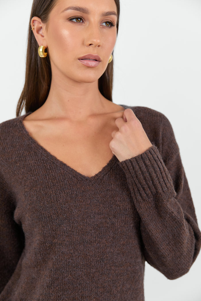 Woman wearing a chocolate brown knit jumper and blue jeans against a white background