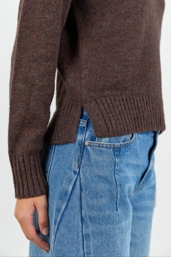Woman wearing a chocolate brown knit jumper and blue jeans against a white background
