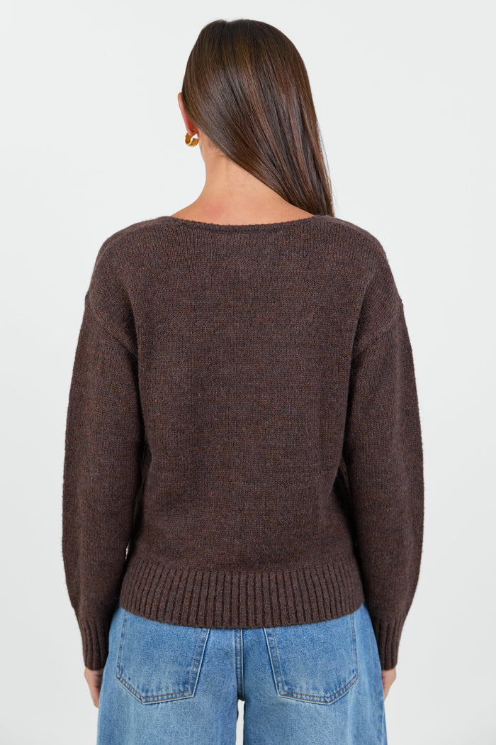 Woman wearing a chocolate brown knit jumper and blue jeans against a white background